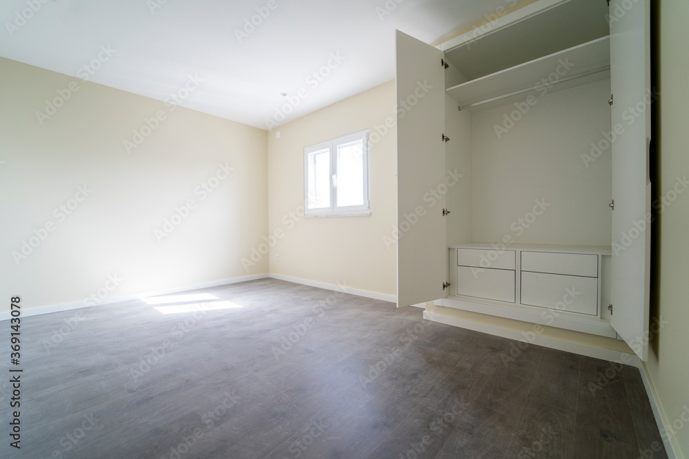 Fototapeta premium Empty room with dark wooden floating laminate flooring and wardrobe. House interior, wide bedroom space. Newly recently painted new apartment or house. Wood floor. Real state and property management