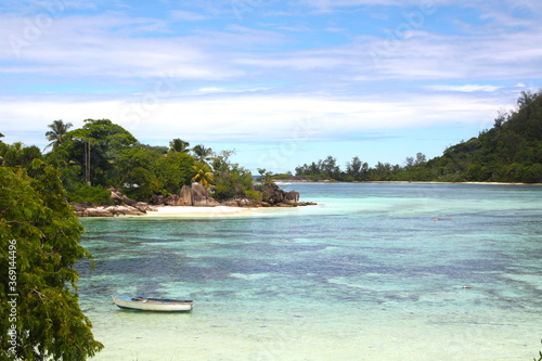 Beautiful wild bay on Seychelles island, with a boat in turquoise blue water sea and white dans beach, granit rocks and green vegetation.