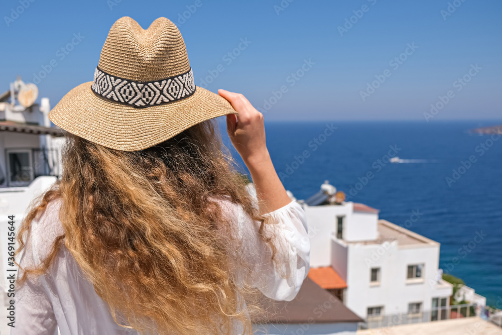 Beautiful young woman in white dress straw hat on white terrace balcony of house or hotel with Sea View