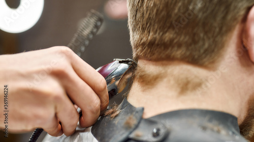 Close up shot of a professional barber working with hair clipper, serving client. Focus on a head