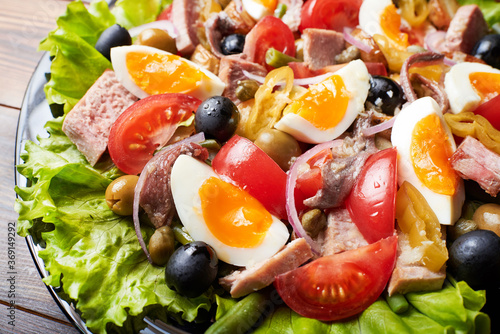 A large platter of tuna salad (nicoise) stands on a wooden table.