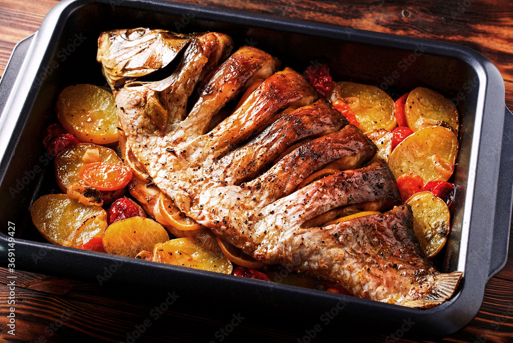 Delicious fried fish (carp) lies on a tray with pieces of potatoes, onions and herbs.