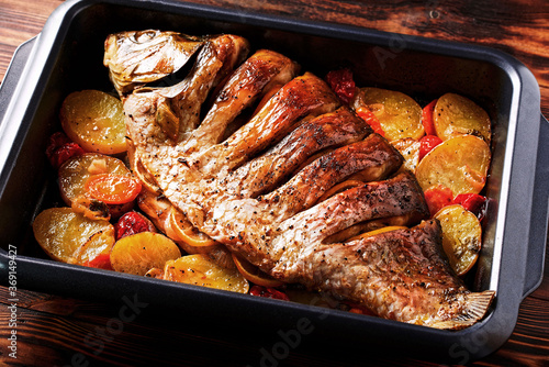 Delicious fried fish (carp) lies on a tray with pieces of potatoes, onions and herbs.