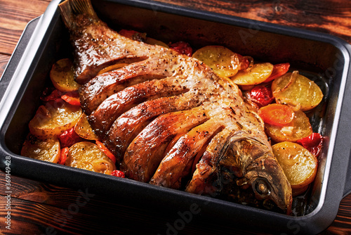 Delicious fried fish (carp) lies on a tray with pieces of potatoes, onions and herbs.
