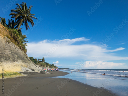 tropical beach in ladrilleros, colombia. Pacific dark sand and yellow clay cliffs with a blue sky at background photo