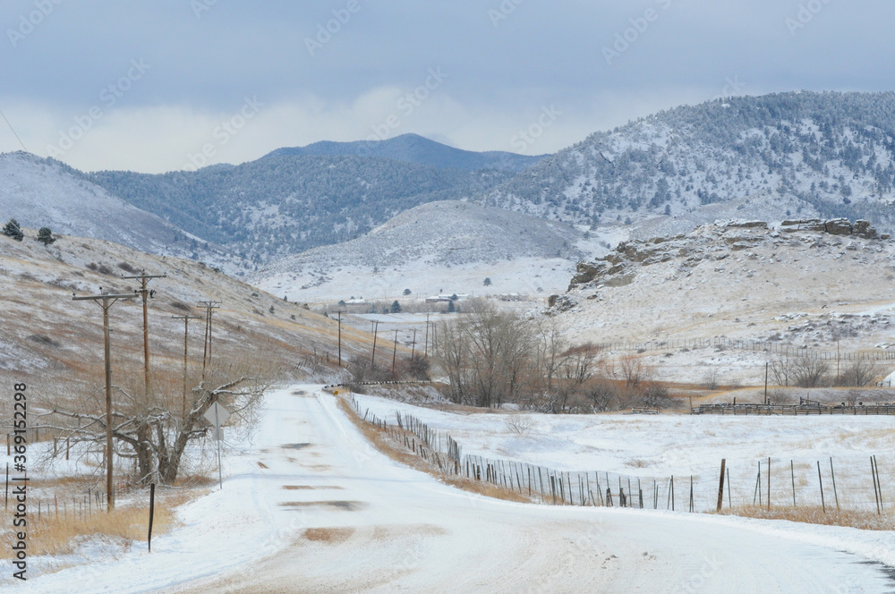 Rural Colorado snow landscape with Rocky Mountain foothills, snow covered road, telephone polls and fences
