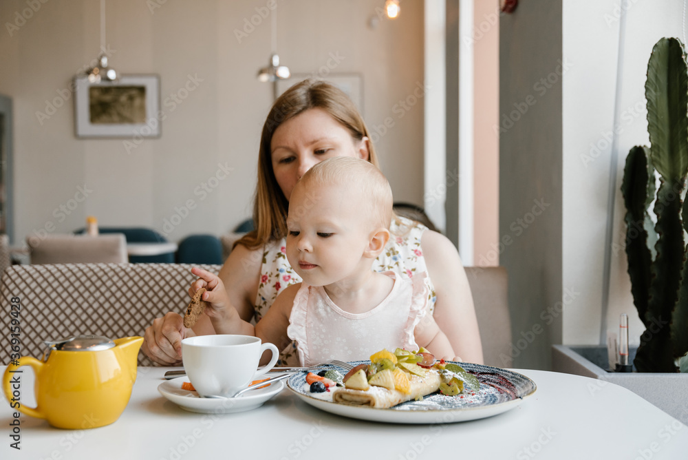 Cute baby girl having breakfast with mother in cafe. Cute baby girl having breakfast with mother in cafe.