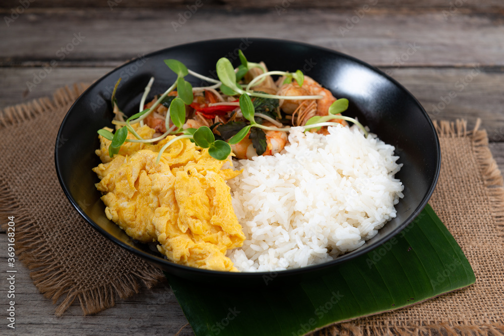 Rice topped with stir-fried shrimp and basil, and fried eggs in white dish. Rice topped with stir-fried shrimp and basil, and fried eggs in white dish.