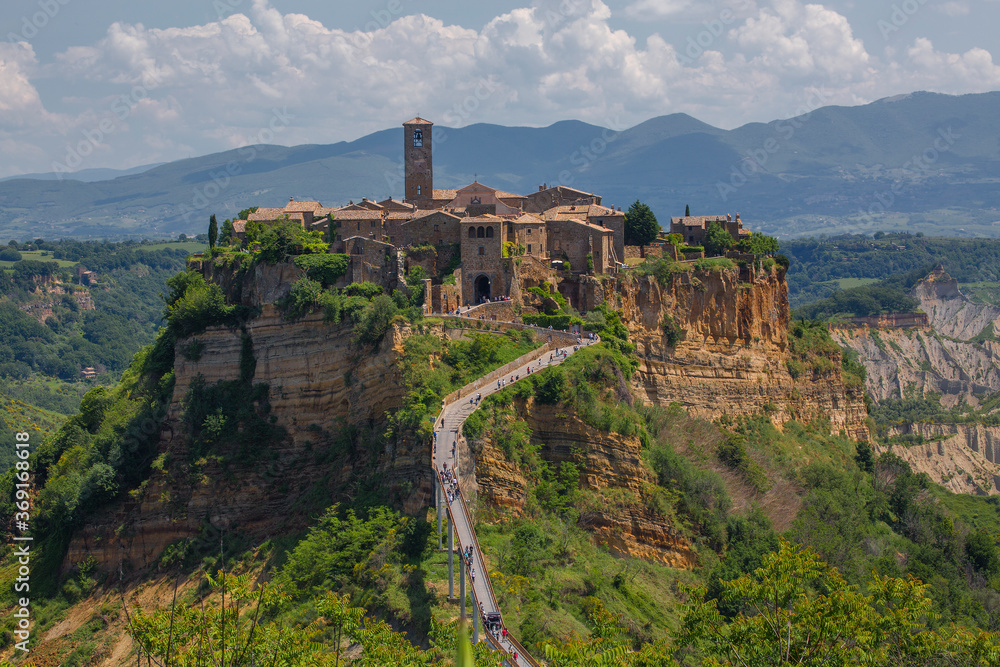 Fototapeta premium Tourists walk along a small bridge to get to the beautiful medieval hill town of Civita di Bagnoregio, located in the Tuscany region of Italy.