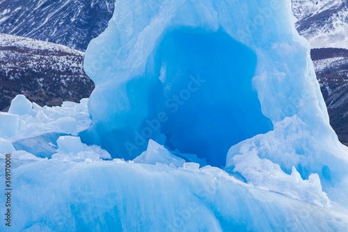 Small ice cave on a floating iceberg at Perito Moreto Glacier , Argentina. Beautiful turquoise color and frozen rocky mountains with snow on the background.