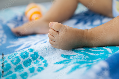 Infant legs of a baby girl sitting on a beach towel at summer time, natural light