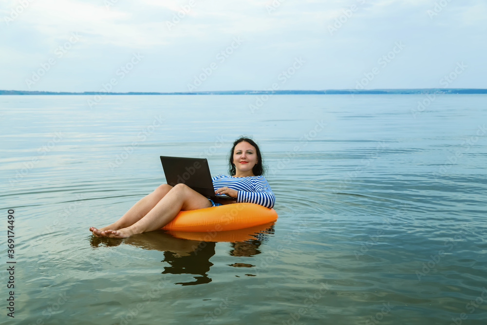 Woman works remotely with laptop in a swimming circle in water.