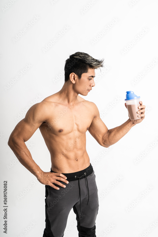 man with muscular body holding a bottle with one hand on waist stand facing side on isolated background man with muscular body holding a bottle with one hand on waist stand facing side on isolated background