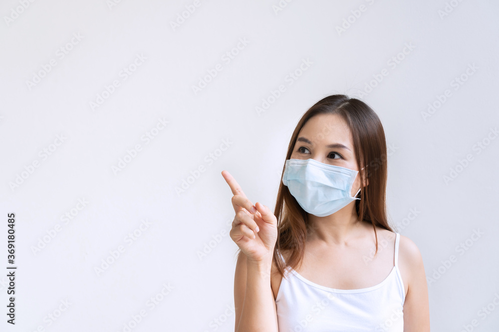 Closeup portrait of beautiful young Asian woman with ptrotective face mask pointing with index finger upwards, isolated on white background. Positive thinking concept. Copy space Closeup portrait of beautiful young Asian woman with ptrotective face mask pointing with index finger upwards, isolated on white background. Positive thinking concept. Copy space