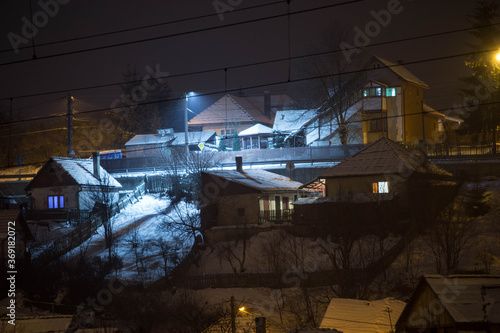 Mountain houses in winter during night with rooftops covered by snow and smoke coming through chimney 