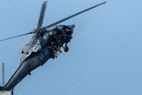 Fototapeta Naklejka Na Ścianę i Meble -  Military combat and war with helicopter flying into the chaos and destruction. Soldiers suspend shooting machine guns with shell flying. Military concept of power, force, strength, air raid. 