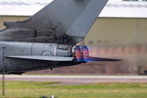 Afterburners glowing on an air force fighter jet aircraft as it speeds down the runway of an air base.