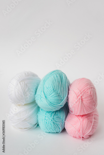 acrylic soft pastel pink, azure and white colored wool yarn thread skeins row on white background, side view, vertical stock photo image with copy space for text