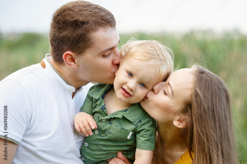 Family life. Portrait of parents and their son on the background of nature. Parents kiss their son. Happy family leisure outdoors. Family life. Portrait of parents and their son on the background of nature. Parents kiss their son. Happy family leisure outdoors.