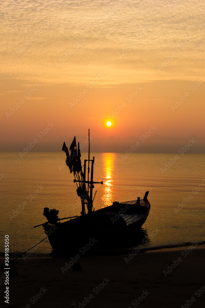 Silhouette of a fishing boat bound on a beach with sunrise in the morning, fresh orange sky.