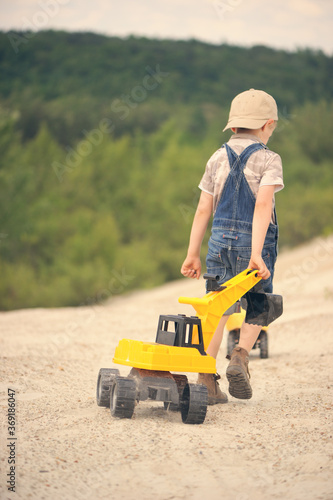 Child, little boy have fun with toy excavator and dumper in the sand. Back view. 