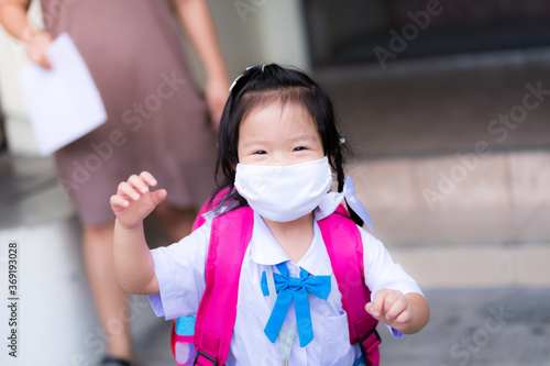 Mother or guardian takes the child back from school. A preschooler ran to see his father carrying a camera with happiness and a smile under a white cloth mask. 3-year-old girl carrying a pink backpack