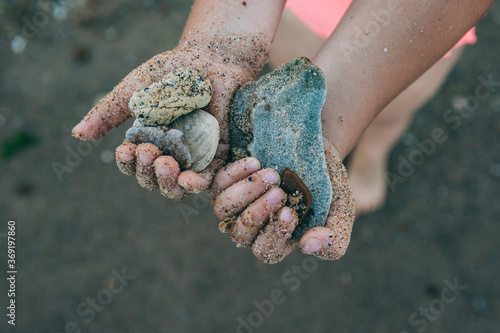 Sea stones in the hands of a child. The hands of a child in the sand hold sea stones on the beach of the Black Sea.