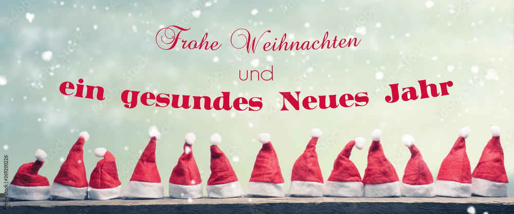 Hats of Santa in a row on a rustic wooden table, Christmas and New Year greetings in German, panoramic view - obrazy, fototapety, plakaty 