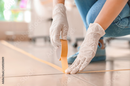 Fotografija Female makeup artist applying a marking tape on floor in salon during coronaviru