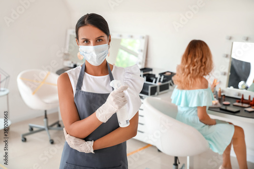 Female makeup artist wearing medical mask in salon during coronavirus epidemic
