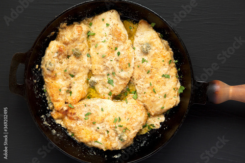 Homemade Italian Chicken Piccata in a cast iron pan on a black background, top view. Flat lay, overhead, from above.