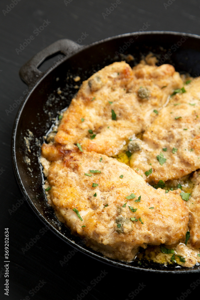 Homemade Italian Chicken Piccata in a cast iron pan on a black surface, low angle view. Close-up. Homemade Italian Chicken Piccata in a cast iron pan on a black surface, low angle view. Close-up.