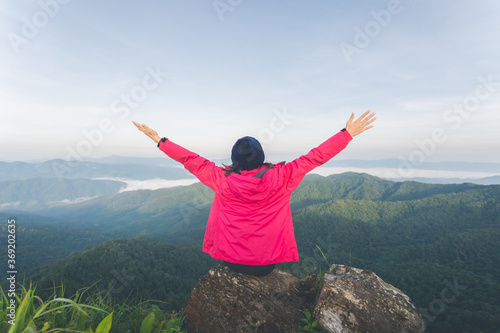 rear of young woman sitting on rock and see view on top mountain, view point with blue sky and mist on mountain at morning light. soft focus.