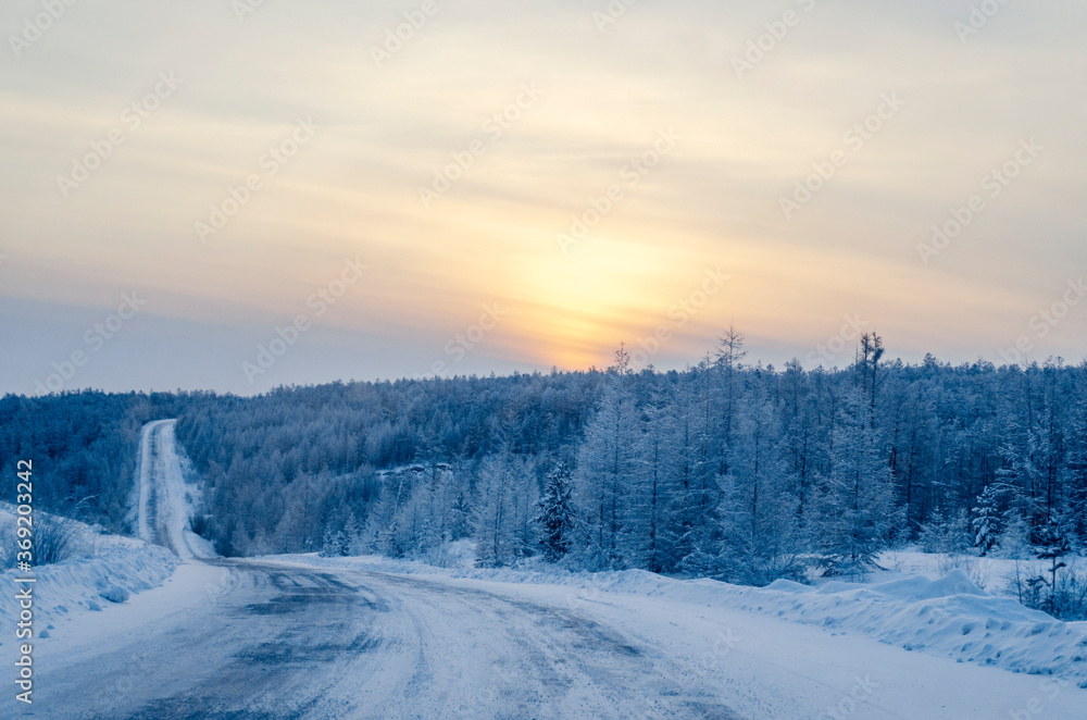 The R504 Kolyma Highway is also known as the Road of Bones. Winter road on a sunset background, disappearing into the sky. On the sides of the road there is the snow-covered forest. Sakha Republic. The R504 Kolyma Highway is also known as the Road of Bones. Winter road on a sunset background, disappearing into the sky. On the sides of the road there is the snow-covered forest. Sakha Republic.