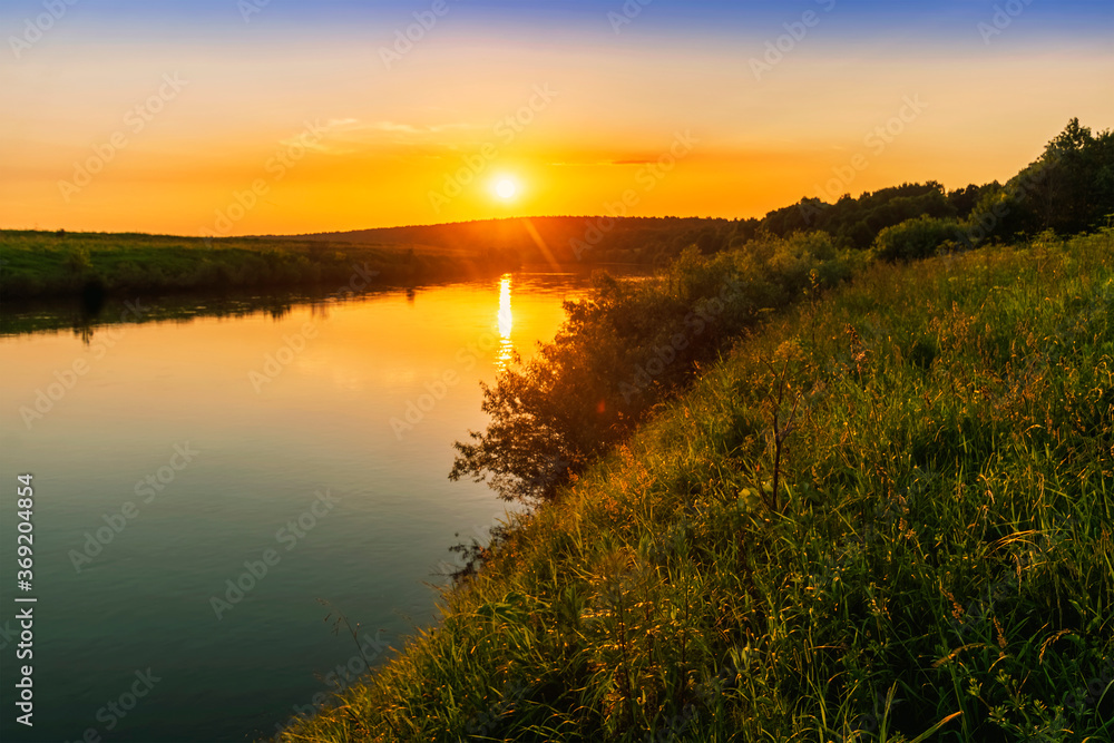 Scenic view at beautiful spring sunset with reflection on a shiny lake with green reeds, bushes, grass, golden sun rays, calm water , sky and glow on a background, spring evening landscape