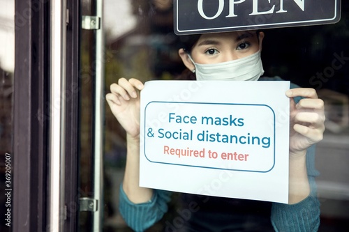 woman holding sign saying face mask and social distancing are required