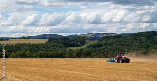 red tractor pulling a blue field cultivator across a harvested wheat field © makasana photo