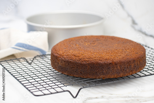 Homemade freshly baked cake cooling on wire rack with round cake pan in background, selective focus