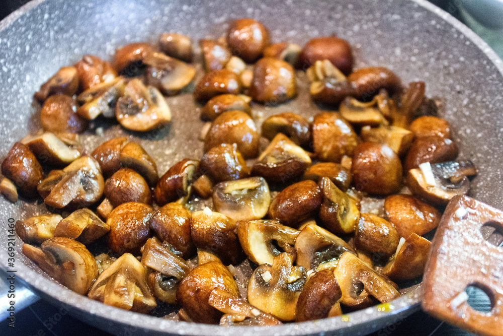 Sauteed in olive oil small champignons with chopped garlic. Mushroom cooking in frying pan.