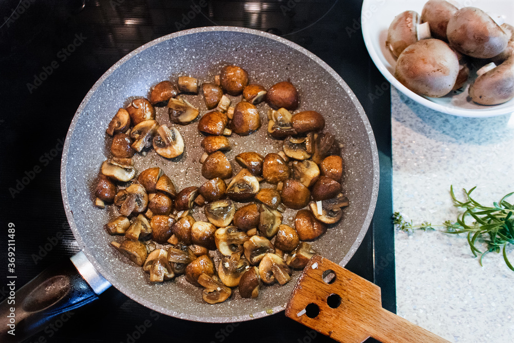 Sauteed in olive oil small champignons with chopped garlic. Mushroom cooking in frying pan top view.