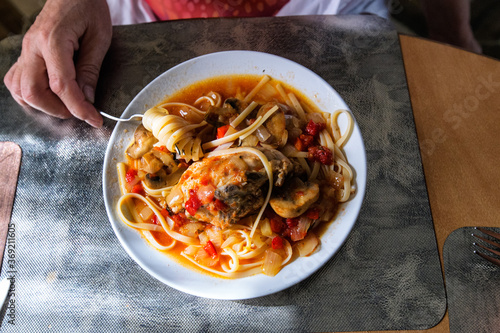 Obraz na płótnie Woman eats homemade chicken cacciatore with pasta and mushrooms in tomatoe sauce. Plate with chicken spagetti cacciatore on dinning table. Woman's hand with fork.Top view. w salonie