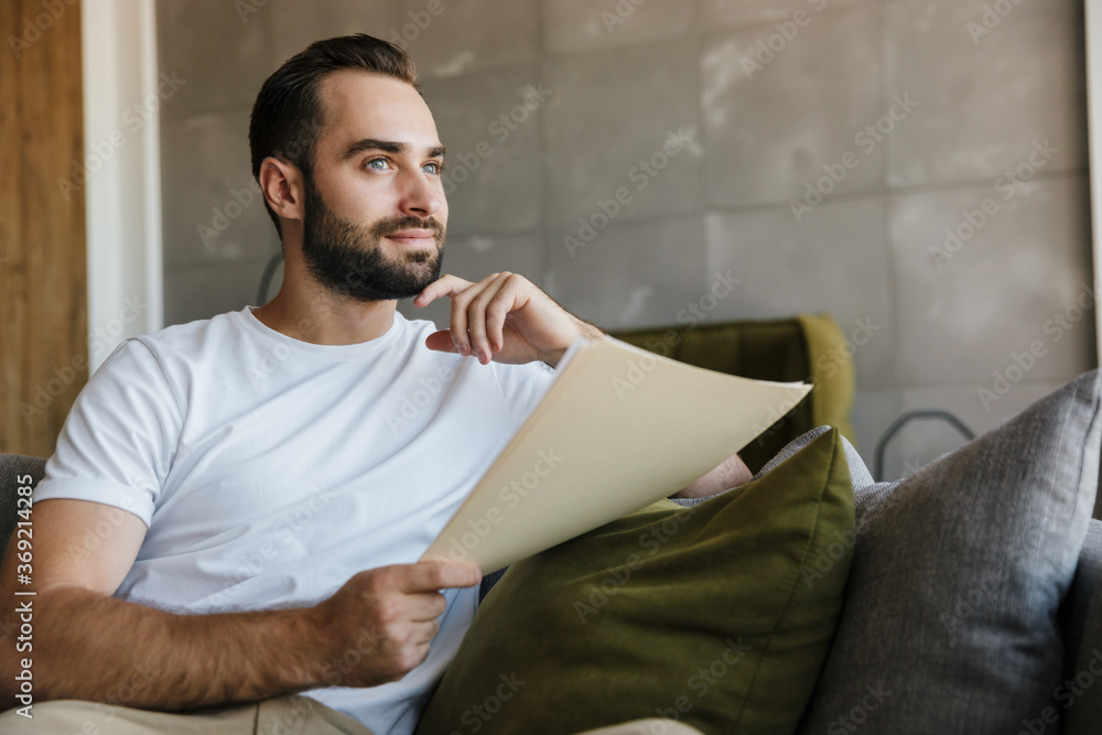 Fototapeta premium Image of young thinking man working with papers while sitting on couch