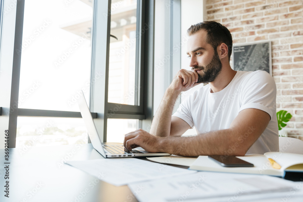Fototapeta premium Image of young man working with laptop while sitting at table