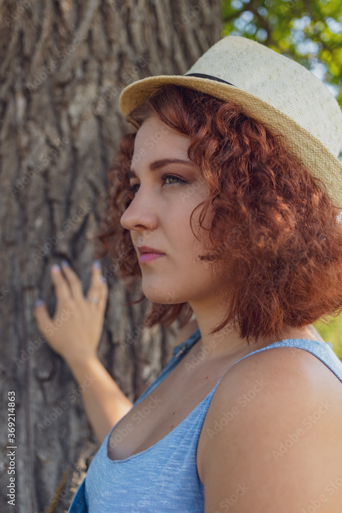 red-haired curly-haired girl in a summer braided headgear and jeans dress posing in the village . High quality photo