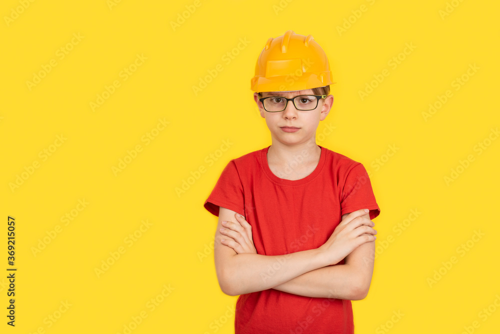 Serious teenager in protective orange hard hat on yellow background. The profession of builder. Copy space