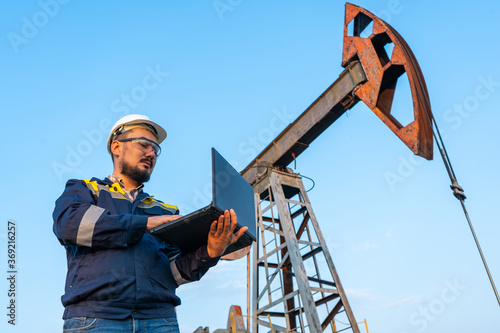 Engineer with a laptop against the background of oil rockers.