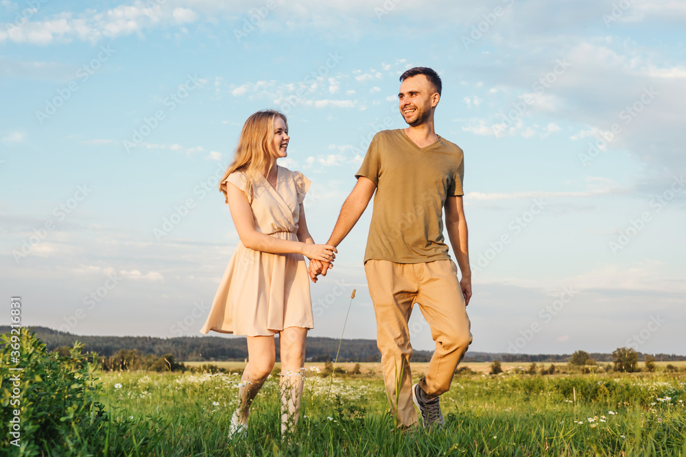 A couple in love walk across the field, talk and smile. Sunset light. Neutral color palette, sky background. A couple in love walk across the field, talk and smile. Sunset light. Neutral color palette, sky background.