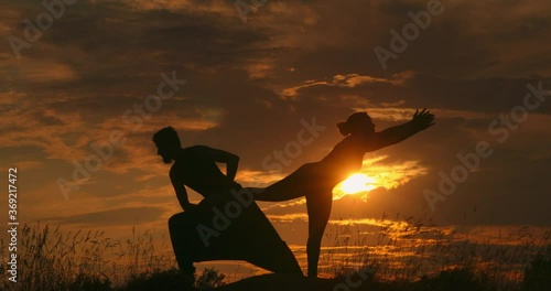 Young sports couple doing acroyoga exercises. Silhouette young couple practicing yoga at sunset. Slim woman doing acro yoga. Beautiful couple doing acro yoga. photo