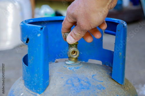 Obraz na plátně Caucasian man opening the valve on blue propan butan gas tank.