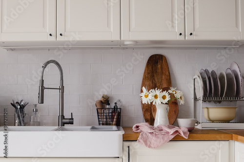 Canvastavla Modern scandinavian style white kitchen with a bunch of chamomile flowers in a jug standing on a towel and miscellaneous kitchen stuff
